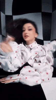 a woman in a white shirt with red hearts on the sleeves is dancing in front of a checkered background .