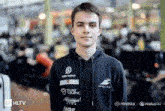 a young man wearing a black hoodie with sponsors on it is standing in front of a crowd .