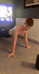 a shirtless boy is doing push ups in front of a tv