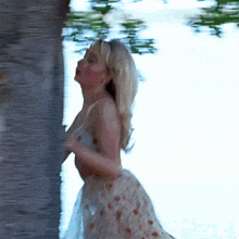 a woman in a floral dress is standing next to a tree