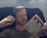 a man sits in a chair reading a book with a barcode on the spine