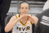 a woman wearing a fever jersey makes a heart with her hands