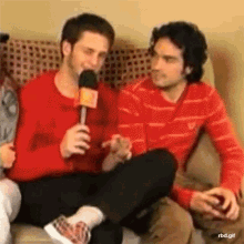 two men are sitting on a couch and one is holding a microphone with rbd.gif written below it