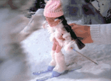 a doll wearing a pink hat is skiing down a snowy slope
