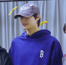 a man wearing a hat and a purple hoodie is standing in front of a curtain .