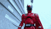 a red superhero with a cape is standing in front of a building .