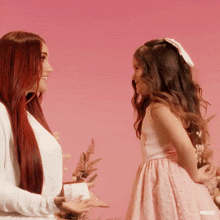 a girl in a pink dress stands next to a woman in a white shirt with rbd30 written on the bottom right