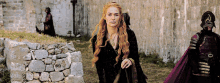 a woman with long red hair is walking in front of a stone wall