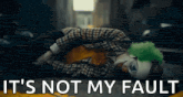 the joker is laying on the ground with the words `` it 's not my fault '' written on the bottom .