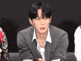 a man in a grey jacket and white shirt is making a funny face while sitting at a table .