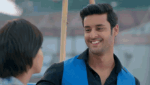a man wearing a blue vest smiles at a woman