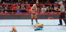 a woman is standing in a wrestling ring next to a man who is laying on the floor .