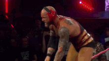 a wrestler in a red and black outfit is standing in a ring