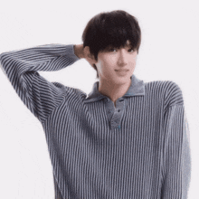 a young man wearing a striped shirt holds his hand behind his head