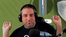 a man wearing headphones stands in front of a microphone with his arms raised in the air