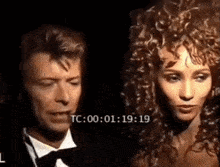 a man in a tuxedo and bow tie is standing next to a woman with curly hair