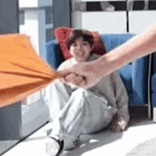 a person is holding an orange umbrella over a child sitting on the floor .