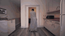 a man wrapped in a blanket is standing in a kitchen next to a refrigerator .