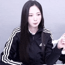 a woman wearing an adidas jacket holds a spoon