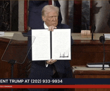 donald trump is holding a signed document in front of a podium