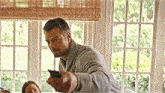 a man is holding a remote control in front of a window while a woman sits on a couch .