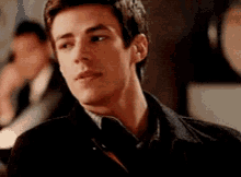 a young man in a black jacket and tie is sitting at a table .