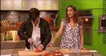 a man is cutting tomatoes on a cutting board while a woman stands behind him .