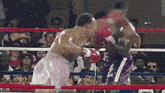 two boxers are fighting in a boxing ring while a crowd watches .
