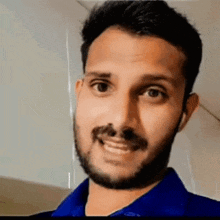 a man with a beard wearing a blue shirt is smiling for the camera .