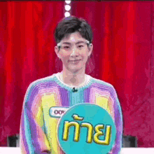 a young man wearing a rainbow sweater is holding a sign with a name tag on it .