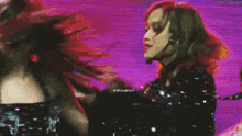 two women with red hair are dancing on a stage with a purple background .