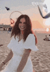 a woman in a white dress is standing on a sandy beach with a ferris wheel in the background .
