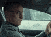 a man wearing glasses is driving a car with a sticker on the windshield that says airbag