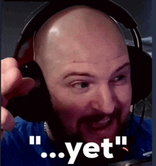 a bald man with a beard wearing headphones with the word yet behind him