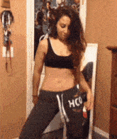 a woman in a crop top and sweatpants is standing in front of a mirror in a bedroom .
