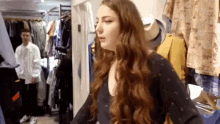 a woman with long red hair is standing in a closet in a clothing store .