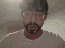 a man with a beard wears a white shirt with the letter t on the front