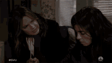 two women hugging in a room with a nbc logo in the corner