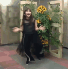 a woman is dancing in front of a plant with sunflowers on it