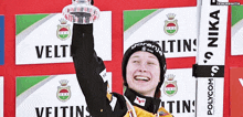a person holding a trophy in front of signs that say veltins and polycom