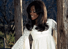 a woman in a white lace dress stands next to a wooden post