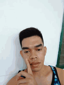 a young man with a blue tank top is holding his nose