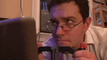 a man wearing glasses is playing a video game on a laptop .