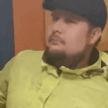 a man with a beard and a hat is wearing a yellow jacket and a black hat .