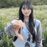 a woman is standing in a field of flowers and giving a thumbs down sign .