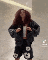 a woman with curly hair is wearing a black jacket and black shorts .