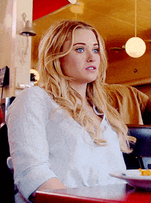 a woman with blonde hair and blue eyes sits at a table