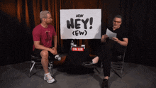 two men are sitting in front of a sign that says hey ( ew )