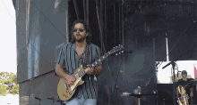 a man in a striped shirt is playing a gibson guitar on stage