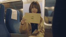 a woman is sitting on a train holding a piece of paper with a picture on it .